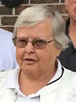 An older woman named Marilyn, wearing glasses and a white shirt, poses for the camera.