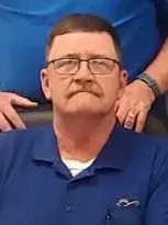 A man in a blue shirt, Pat Fay, sitting in a chair.