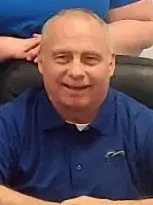 A man named Tony Ball, who is dressed in a blue shirt smiling ar camera.