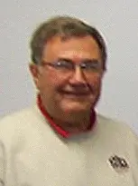 Gary Schon, Board of Planning & Zoning, wearing glasses and a sweater, poses in front of a wall.